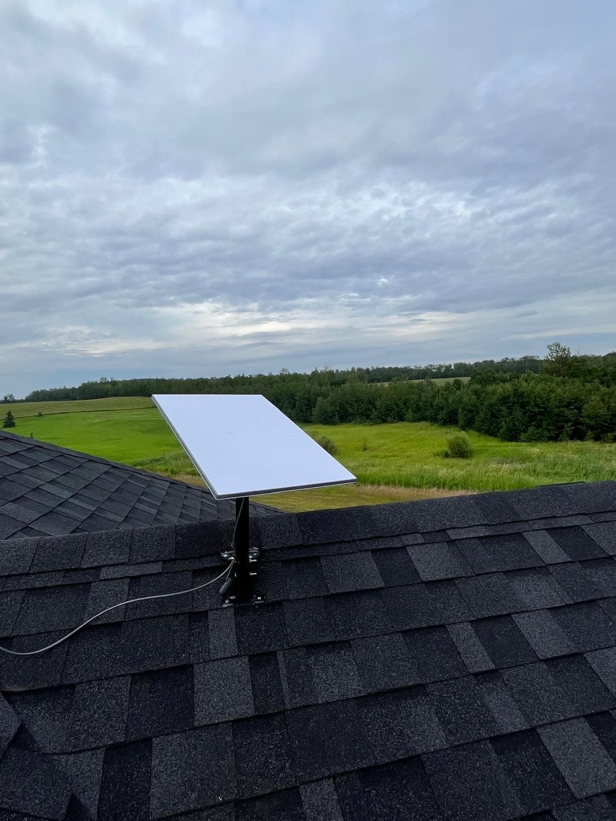 Starlink dish mounted on the ridge of a shingled roof overlooking rolling farmland and a treeline